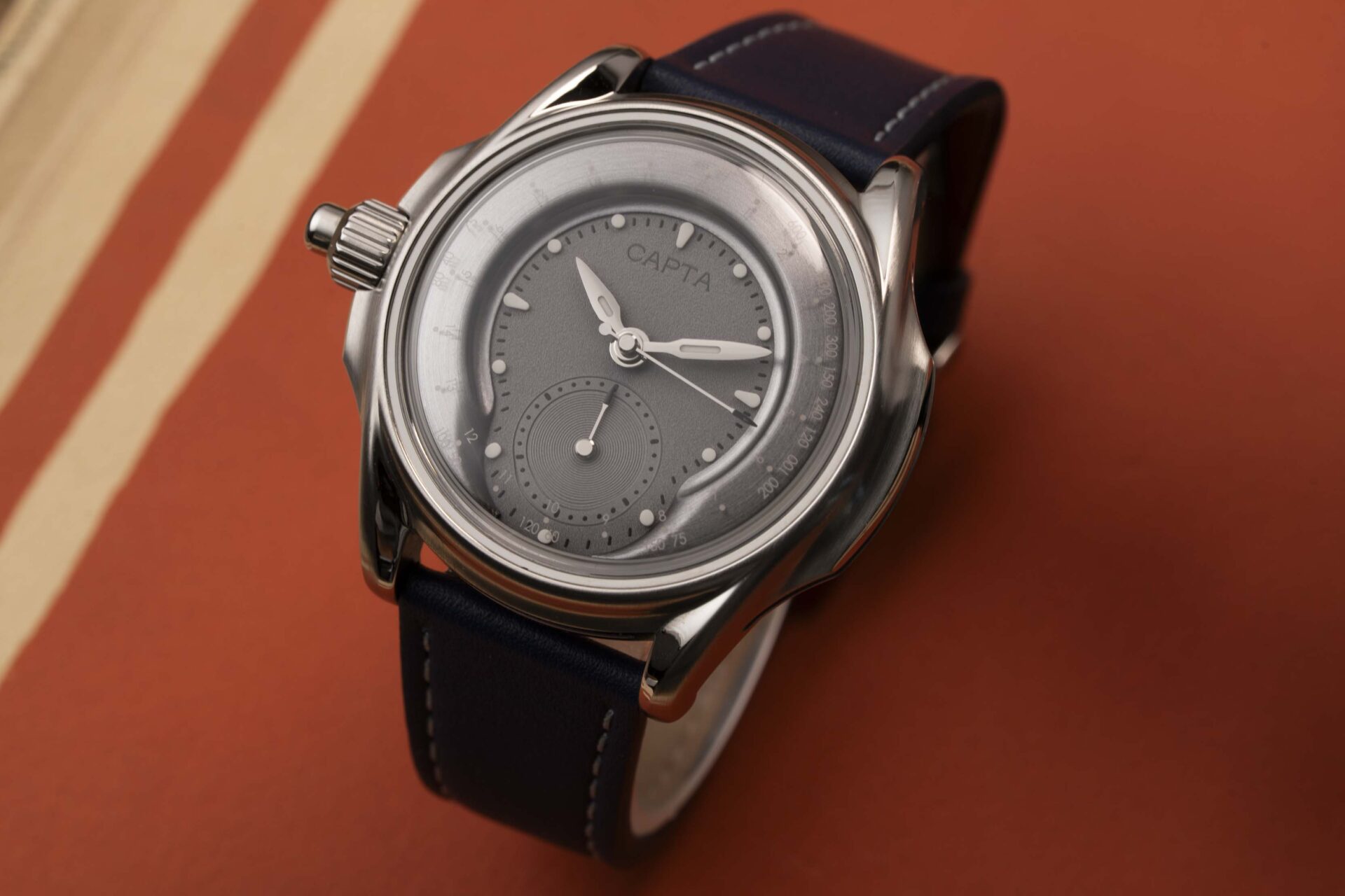 Montre française Capta Omnia Uniscale cadran gris et bracelet cuir bleu marine sur fond orange